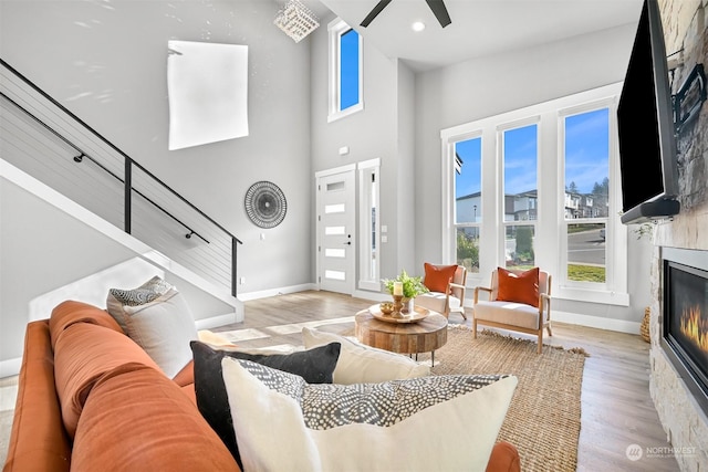 living room with ceiling fan, a towering ceiling, and light hardwood / wood-style floors