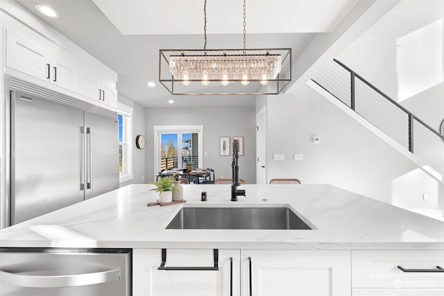 kitchen with sink, light stone counters, stainless steel built in fridge, pendant lighting, and white cabinets