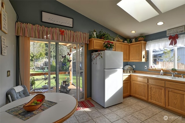 kitchen featuring sink, light tile patterned floors, lofted ceiling with skylight, and white fridge