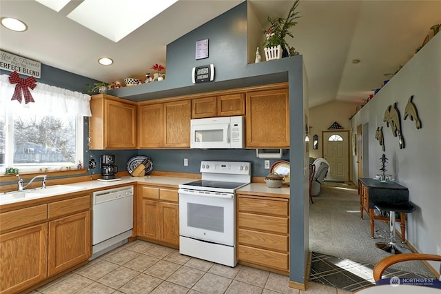 kitchen with sink, white appliances, lofted ceiling with skylight, and light tile patterned floors