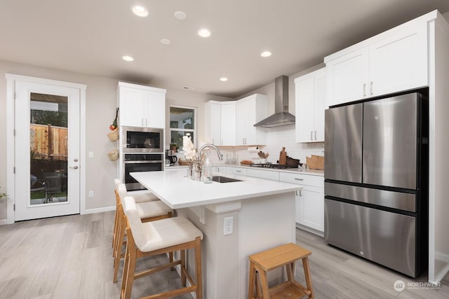 kitchen featuring wall chimney exhaust hood, sink, a breakfast bar area, appliances with stainless steel finishes, and an island with sink