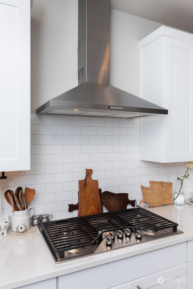 kitchen with stainless steel gas stovetop, white cabinetry, tasteful backsplash, and wall chimney exhaust hood