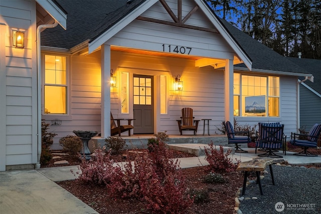 view of exterior entry featuring covered porch and roof with shingles