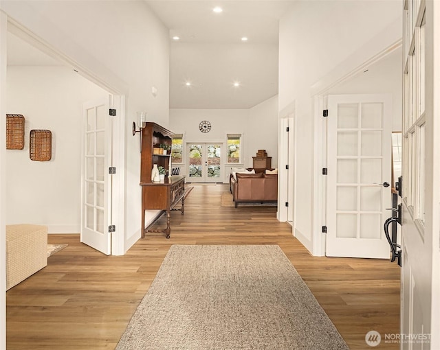 foyer entrance featuring light wood finished floors, baseboards, a high ceiling, french doors, and recessed lighting