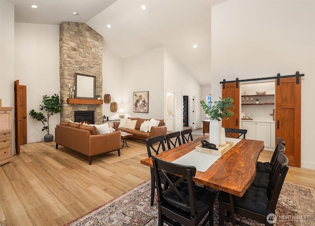 dining space with high vaulted ceiling, a barn door, recessed lighting, a fireplace, and light wood finished floors