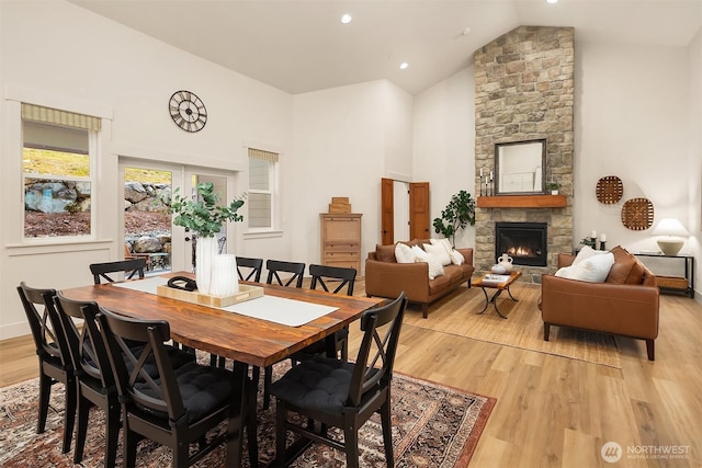 dining space featuring baseboards, a stone fireplace, light wood-type flooring, high vaulted ceiling, and recessed lighting