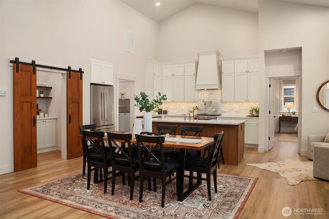 dining space with high vaulted ceiling, light wood-style flooring, and a barn door