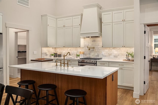 kitchen with stainless steel range, a kitchen breakfast bar, a kitchen island with sink, light countertops, and premium range hood