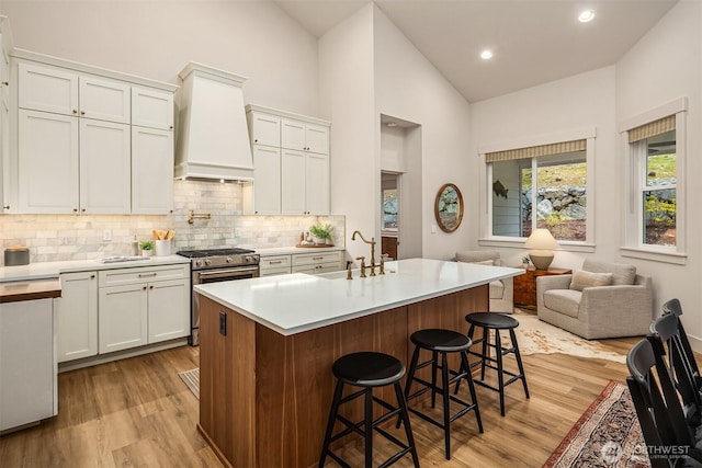 kitchen featuring light countertops, a kitchen island with sink, a sink, premium range hood, and a kitchen breakfast bar