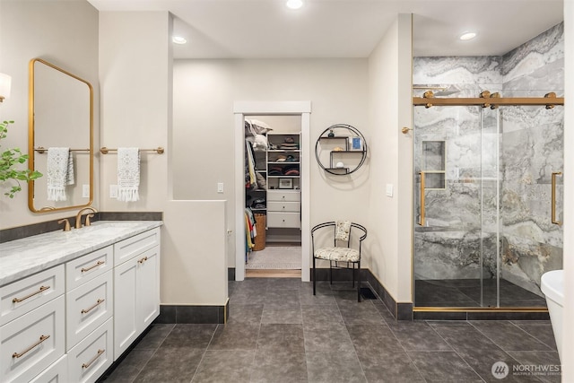 bathroom with a shower stall, baseboards, a walk in closet, and vanity