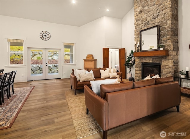 living area featuring light wood finished floors, baseboards, french doors, a high ceiling, and a stone fireplace