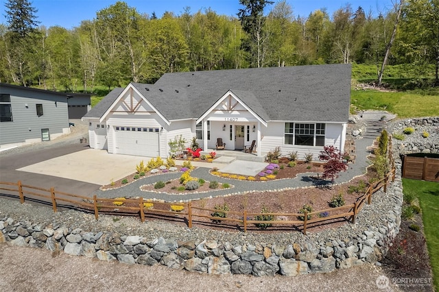 view of front of property featuring an attached garage, a shingled roof, a fenced front yard, and driveway