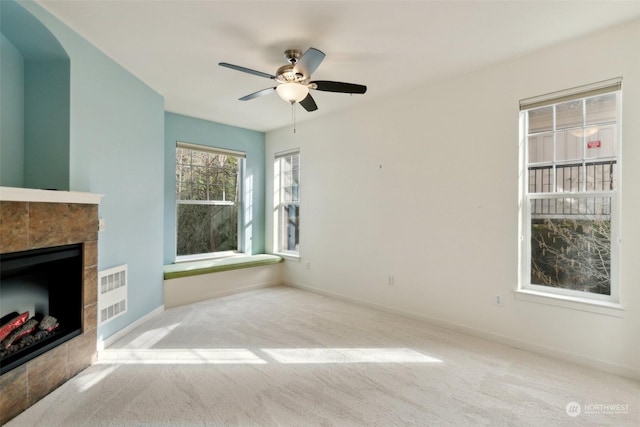 unfurnished living room with ceiling fan, a tile fireplace, and light carpet