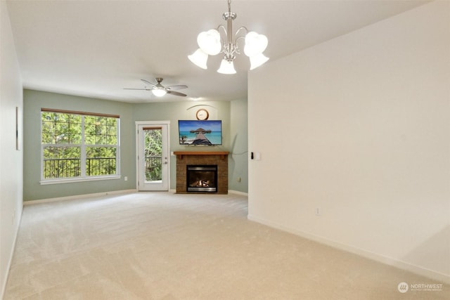 unfurnished living room with ceiling fan with notable chandelier, a tile fireplace, and light carpet