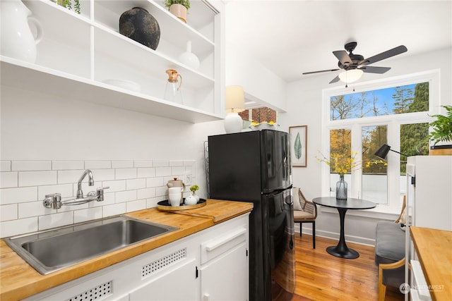 kitchen featuring butcher block counters, sink, decorative backsplash, and black refrigerator