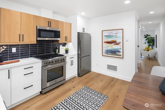 kitchen featuring high end appliances, decorative backsplash, white cabinets, and light wood-type flooring