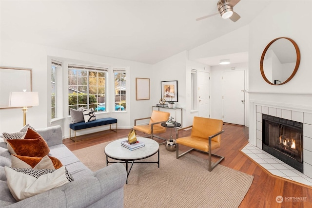 living room with vaulted ceiling, a tile fireplace, light hardwood / wood-style floors, and ceiling fan