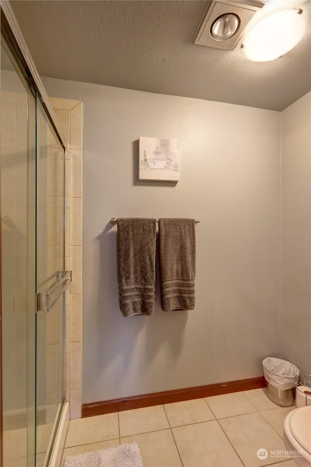 bathroom featuring tile patterned floors, toilet, an enclosed shower, and a textured ceiling