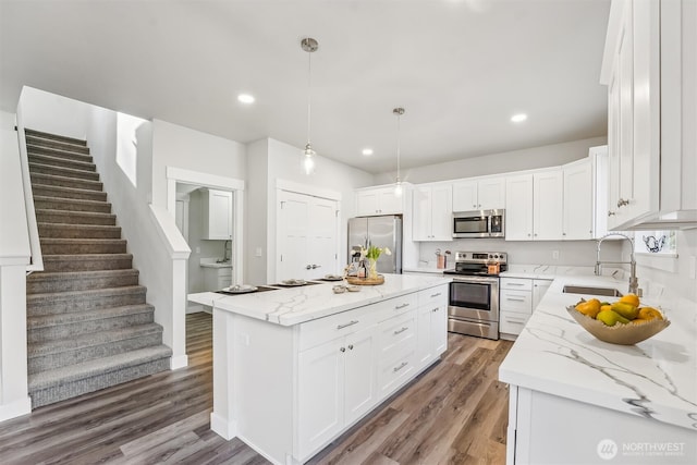 kitchen featuring a sink, a kitchen island, white cabinets, appliances with stainless steel finishes, and decorative light fixtures