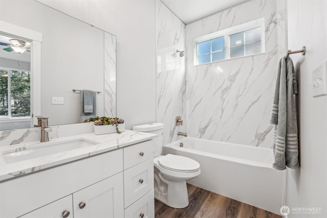 bathroom with ceiling fan, toilet, wood finished floors, vanity, and  shower combination