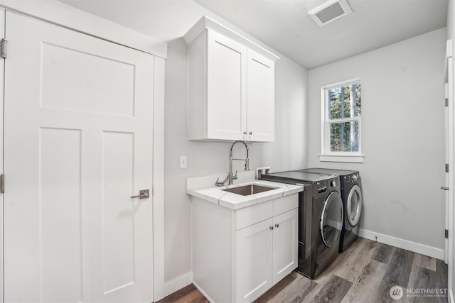 laundry area with cabinet space, visible vents, washing machine and dryer, a sink, and wood finished floors