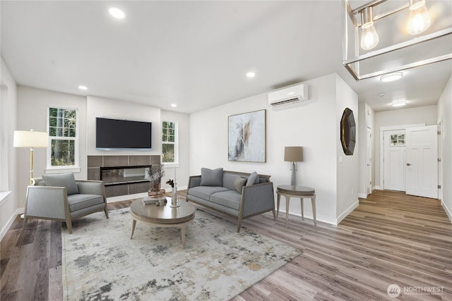 living area with a wall mounted AC, a fireplace, wood finished floors, and a wealth of natural light