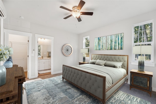 bedroom with ensuite bath, baseboards, a ceiling fan, and a wall mounted air conditioner