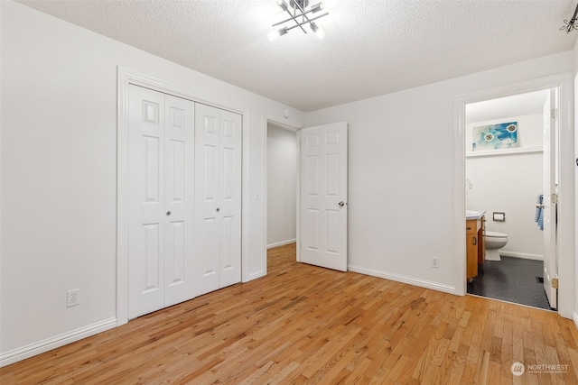 unfurnished bedroom with ensuite bath, a textured ceiling, a closet, and light wood-type flooring