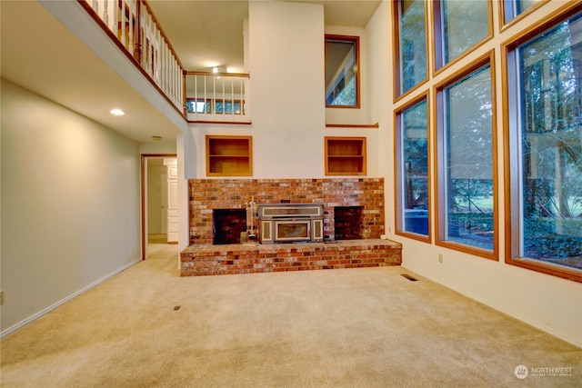 unfurnished living room with a healthy amount of sunlight, a fireplace, a high ceiling, and carpet