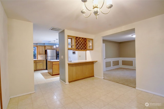 kitchen featuring sink, an inviting chandelier, hanging light fixtures, stainless steel refrigerator, and kitchen peninsula