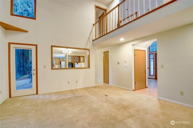 unfurnished living room featuring a towering ceiling, light carpet, and a notable chandelier