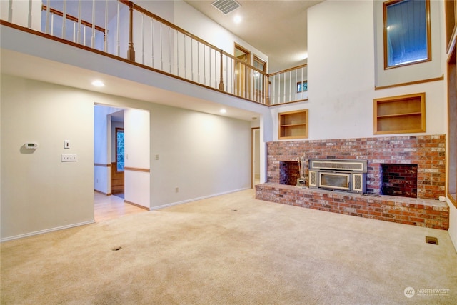 unfurnished living room with a towering ceiling, light colored carpet, built in features, and a fireplace