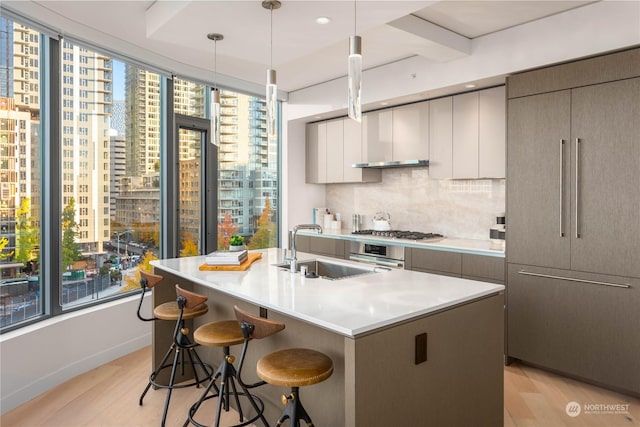 kitchen with sink, appliances with stainless steel finishes, backsplash, hanging light fixtures, and a center island with sink