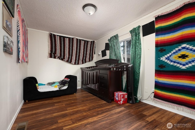 bedroom with dark wood-style floors, a nursery area, visible vents, and a textured ceiling