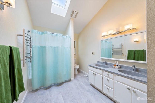 bathroom with toilet, tile patterned floors, vanity, and vaulted ceiling with skylight