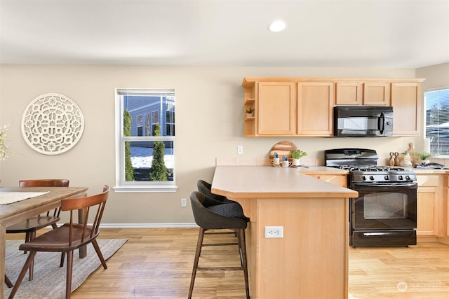 kitchen featuring a kitchen breakfast bar, kitchen peninsula, light brown cabinetry, and black appliances