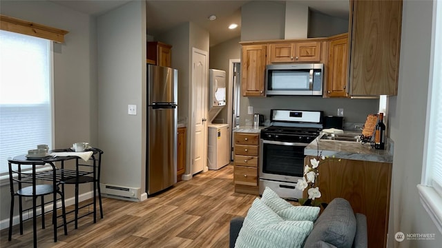 kitchen featuring lofted ceiling, stacked washer and dryer, appliances with stainless steel finishes, a baseboard radiator, and light wood-type flooring