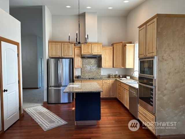 kitchen with appliances with stainless steel finishes, pendant lighting, sink, a center island, and light stone counters