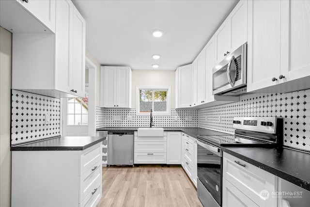 kitchen with sink, white cabinetry, light wood-type flooring, appliances with stainless steel finishes, and backsplash