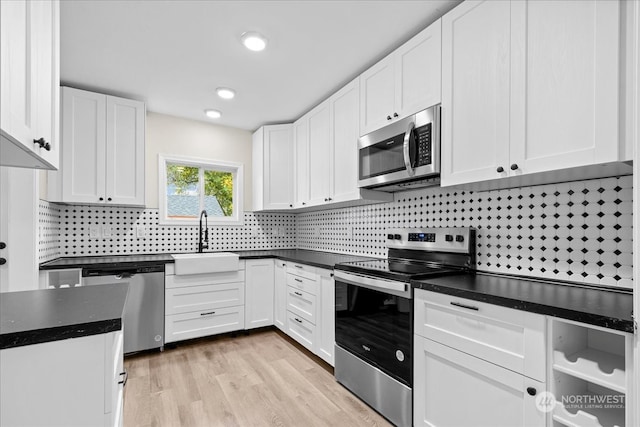 kitchen featuring sink, white cabinets, stainless steel appliances, light hardwood / wood-style floors, and backsplash