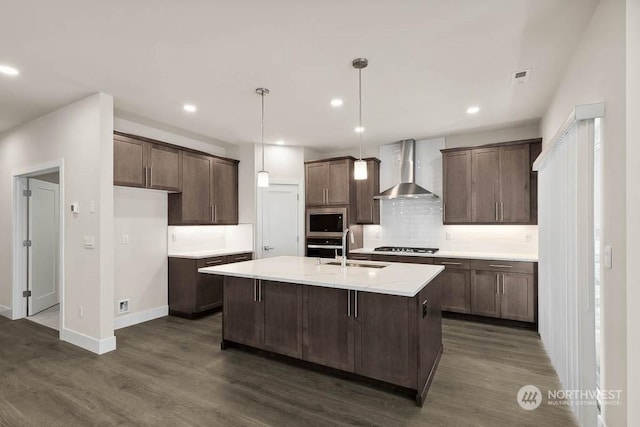 kitchen featuring pendant lighting, sink, a kitchen island with sink, stainless steel appliances, and wall chimney range hood