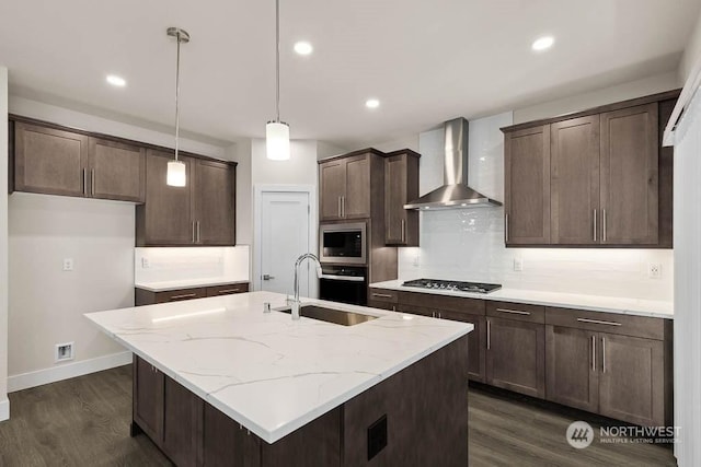 kitchen with pendant lighting, wall chimney range hood, sink, appliances with stainless steel finishes, and light stone countertops