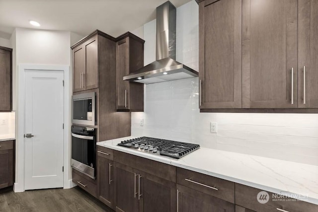 kitchen featuring dark wood-type flooring, dark brown cabinets, wall chimney range hood, stainless steel appliances, and backsplash