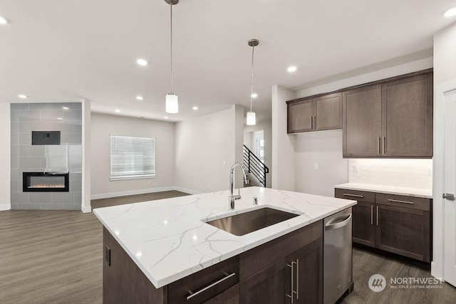 kitchen featuring sink, light stone counters, stainless steel dishwasher, a tile fireplace, and a kitchen island with sink