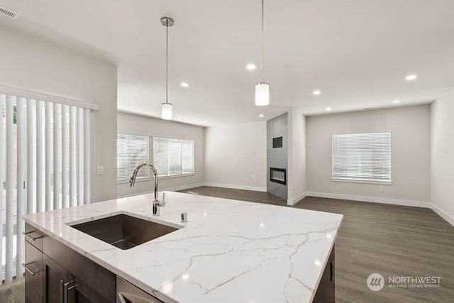 kitchen featuring dark wood-type flooring, sink, hanging light fixtures, a fireplace, and light stone countertops