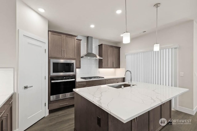 kitchen featuring pendant lighting, wall chimney range hood, sink, stainless steel appliances, and light stone counters