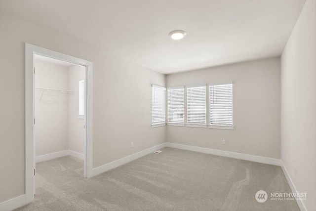 unfurnished bedroom with a walk in closet, light carpet, and a closet