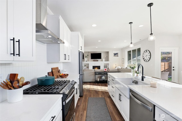 kitchen with sink, white cabinets, hanging light fixtures, stainless steel appliances, and wall chimney exhaust hood