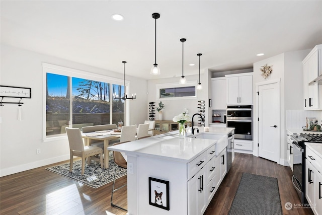 kitchen featuring pendant lighting, sink, white cabinets, stove, and a kitchen island with sink