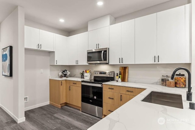 kitchen featuring appliances with stainless steel finishes, dark hardwood / wood-style floors, sink, white cabinets, and light stone countertops